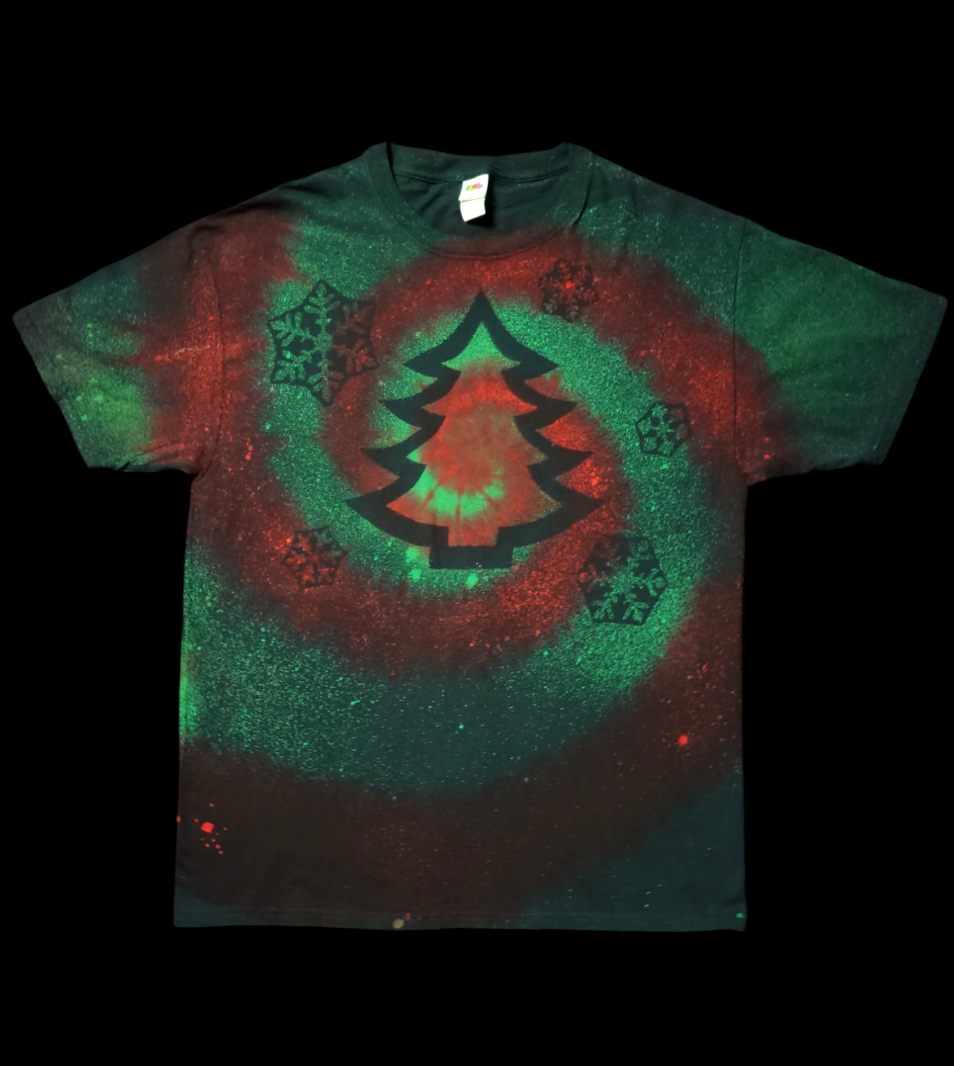 Front view of t-shirt with large Christmas tree printed in the center surrounded by printed snowflakes. Reverse-dye method creates a bright red swirl on a background of greens.