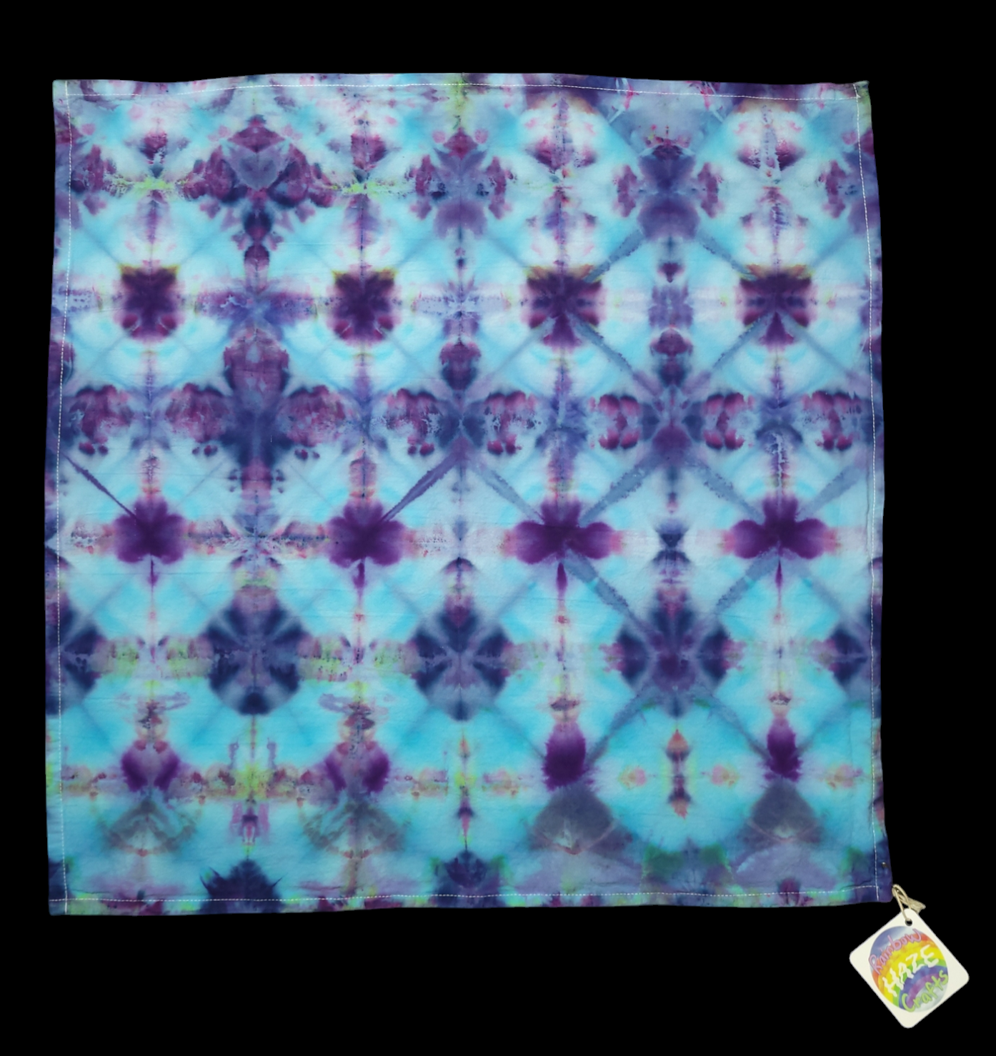 Square kitchen towel dyed in an interconnected series of diamonds with flower-like patterns at the intersections. Colors are blues and purples.