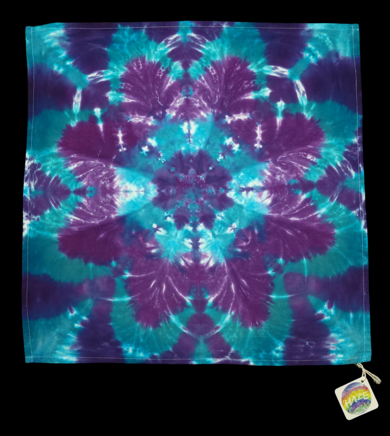 View of kitchen towel with star-like flower design in jewel-toned teals and purples.